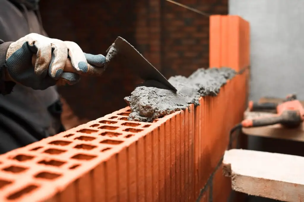 Bricklayer puts bricks to make a wall