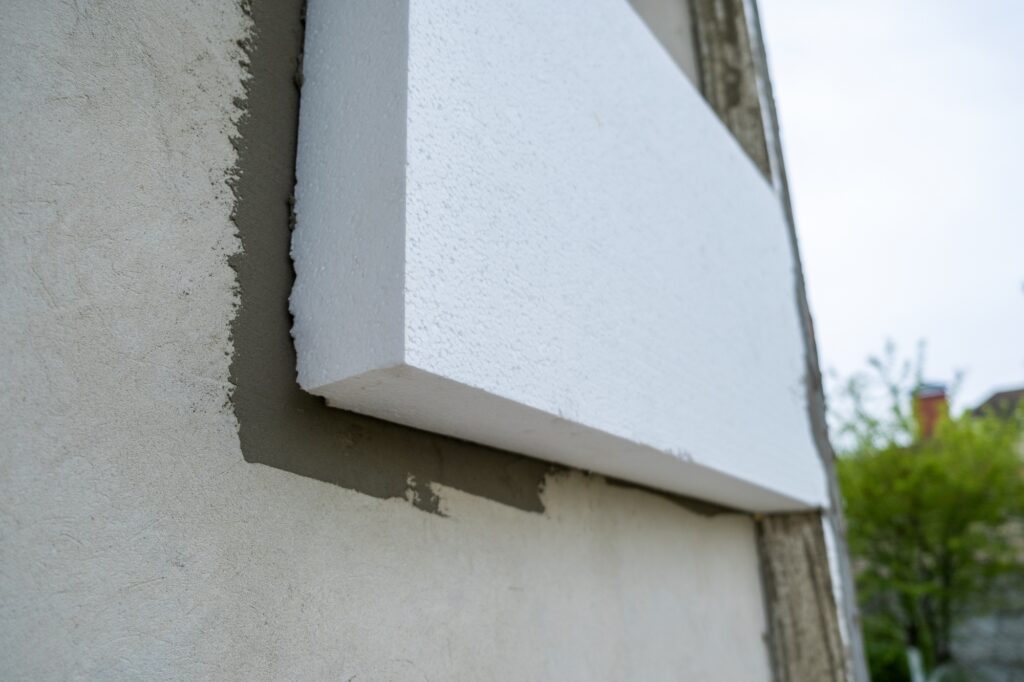 Installation of styrofoam insulation sheets on house facade wall for thermal protection.